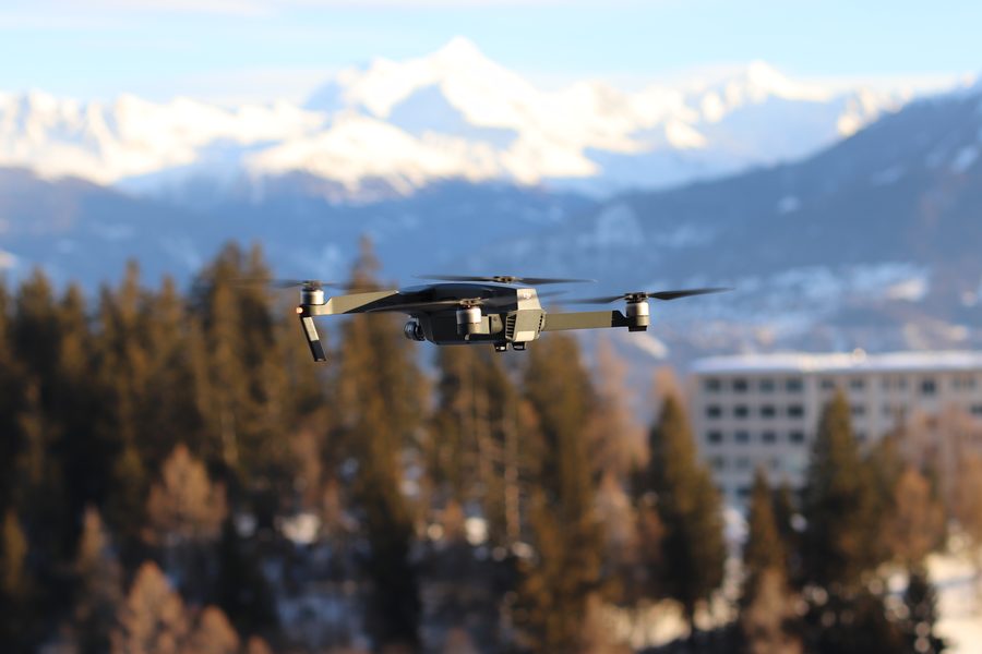 Drone hovering in front of pine trees and snowy mountains